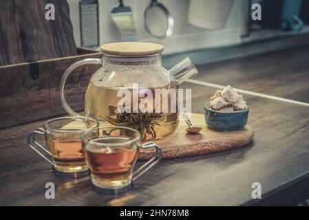 Blooming flowering tea in glass teapot and two cups on kitchen worktop closeup Stock Photo