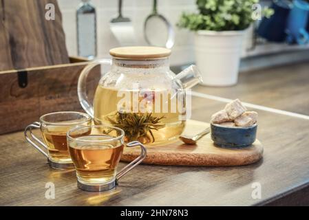 Blooming flowering tea in glass teapot and two cups on kitchen worktop closeup Stock Photo