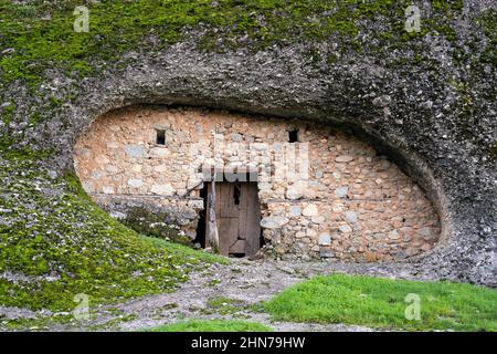 An old dwelling under a hill overgrown with grass and vegetation in the middle, an old door and two small windows. Antique architecture. Ancient house Stock Photo