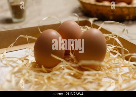 Closeup three eggs. Easter craft box with brown eggs on eco background. Chicken eggs on craft table with hay and straw. Close-up view of raw product Stock Photo