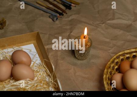 Candle with light. Rustic background. Tools for decorating Paschal eggs, Pysankas. Collection of eggs. Homemade pen and melted beeswax for drawing Stock Photo