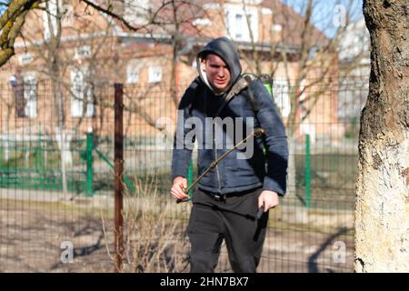 Organic ecological agriculture. Defocus farmer man spraying tree with manual pesticide sprayer against insects in spring garden. Agriculture and Stock Photo