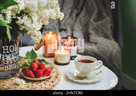Bouquet of purple Lilac flowers on coffee table with cup of tea,  fresh  burning candles in home interior Stock Photo