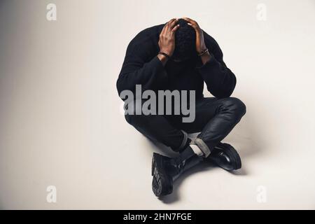 distressed Afroamerican with hands in the back of his head seated white background - full shot. High-quality photo Stock Photo