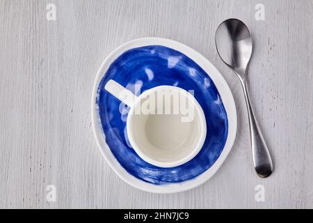 Empty white cup for hot drinks with a spoon on a blue plate on a white wooden table Stock Photo