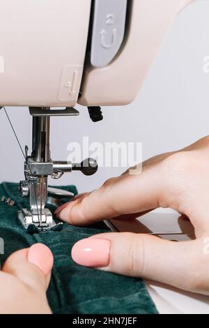 Woman tailor works on sewing machine. Hands hold fabric. World tailors day. Close-up of sewing process. Home clothing repair. Stock Photo