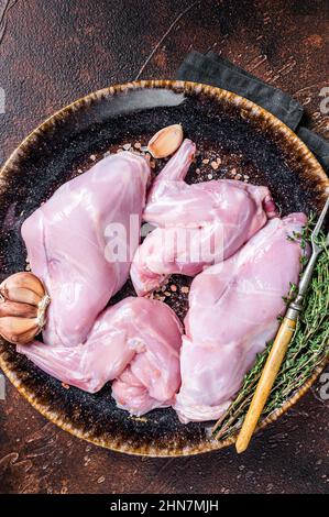 Raw fresh rabbit legs on a plate with herbs. Dark background. Top view Stock Photo