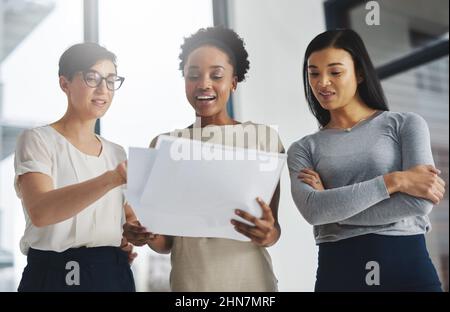 Divide the task, share the success. Shot of a group of businesswomen analyzing paperwork together. Stock Photo