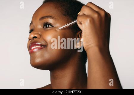 African-american woman dropping serum collagen moisturizer on her face isolated over white background. Cosmetology beauty procedure. Beauty face. Stock Photo