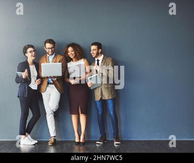 The connected team is an efficient team. Studio shot of a group of businesspeople using wireless technology together while standing in line against a Stock Photo