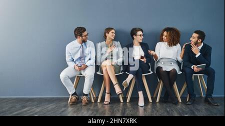 Friendly conversation calms the pre-interview nerves. Studio shot of a group of businesspeople talking while waiting in line against a gray background Stock Photo