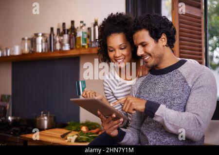 Lets download this recipe. Shot of a young couple using their tablet together while they get ready to prepare a meal. Stock Photo
