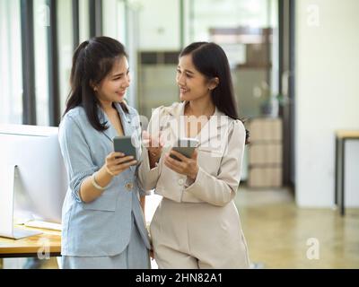 Two young employees discussing working issues or enjoying informal conversation. Employees chatting during coffee break. Stock Photo
