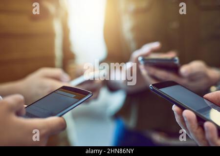 Its one connected world were living in. Cropped shot of a group of colleagues using their smart phones in synchronicity. Stock Photo