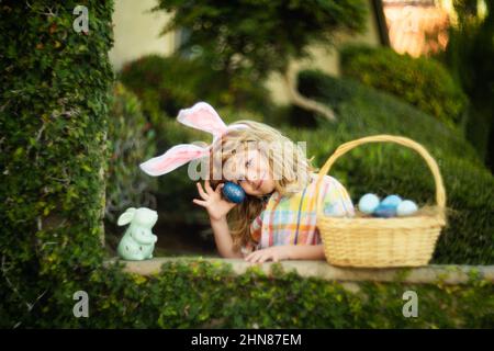 Child hunt egg in garden on Easter day. Kid boy with rabbit ears, portrait of cute boy wear bunny ears with easters basket outdoors, Cute kids hunting Stock Photo
