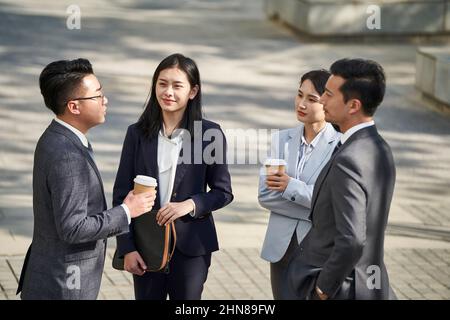 group of four young asian business people standing chatting outdoors on street Stock Photo