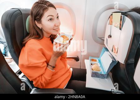 Happy woman ordered tasty dish during the flight in the plane and eats fish with rice. Catering and menu on the airplane Stock Photo