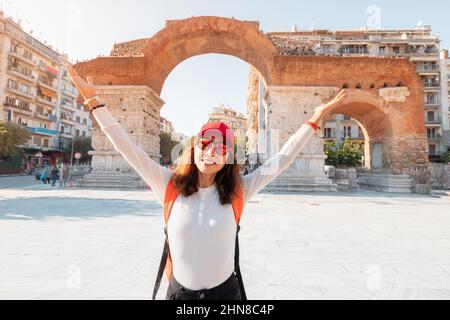 Happy traveler student girl with backpack stands on the viewpoint and enjoys the view of Galerius Arch in Thessaloniki city in Greece Stock Photo