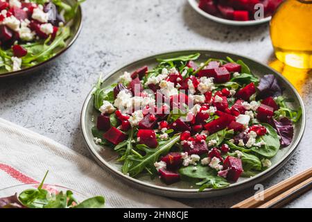 Arugula, Beet and cheese salad with pomegranate and dressing on plate on grey stone kitchen table background, place for text, top view Stock Photo