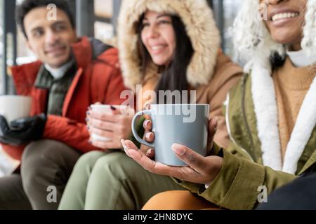 Close-up of woman holding cup of coffee in her hands, she sitting outdoors in winter morning and talking to her friends Stock Photo