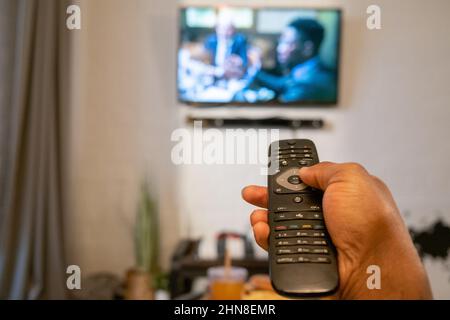 Close-up of man pushing the buttons on remote control to switch the channel on TV in the room Stock Photo