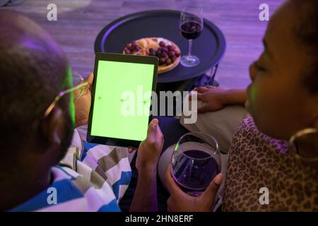 African young couple drinking red wine and using digital tablet, they watching movie online sitting on sofa at home Stock Photo