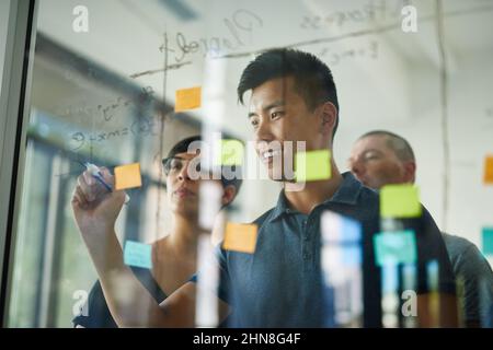 Planning is the first step. Cropped shot of a group of young designers planning on a glass board. Stock Photo