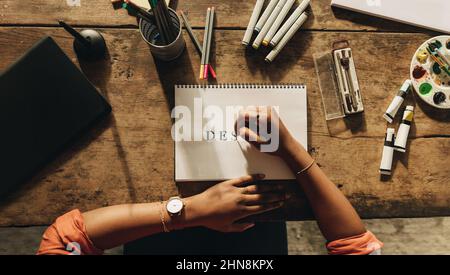 Designer drawing the word "DESIGN" while sitting in her creative workspace. High angle view of a female graphic designer working on a new project. Ano Stock Photo
