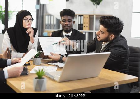 Team of diverse competent financiers showing graphs and charts on laptop during video conference. Company workers having online call with director or colleagues at office. Stock Photo