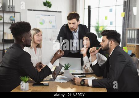 Team of competent financial analysts gathering together at boardroom for brainstorming. Multiracial men and women in formal clothes discussing business plan of common project. Stock Photo