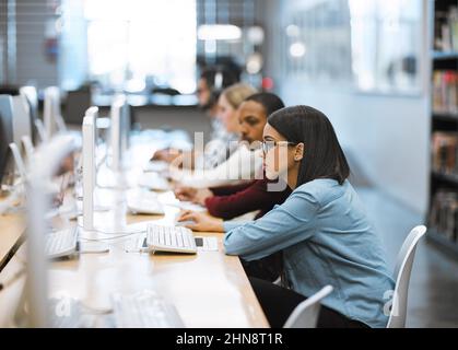 Working hard to complete all their assignments. Shot of a group of university students working on computers in the library at campus. Stock Photo
