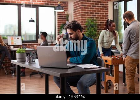 Pensive executive manager having doubtful think about marketing project analyzing company turnover on computer. Businessman working at business collaboration in startup office. Diverse team Stock Photo