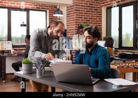 Busy executive managers analysing marketing statistics using laptop computer planning company strategy. Diverse businesspeople working at business collaboration in brick wall startup office Stock Photo