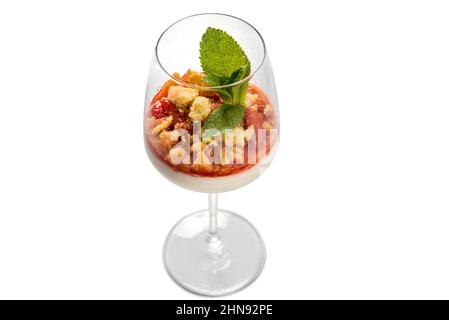 Panna cotta italian dessert with strawberry syrup and crumbled cake with mint leaves in glass goblet glass, top view, isolated on white Stock Photo