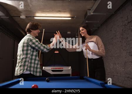 Young couple high fiving each other, celebrating successful pool game Stock Photo