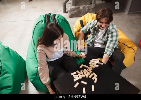 Top view shot of a couple playing wood blocks stacking game, sitting in colorful beanbag chairs Stock Photo