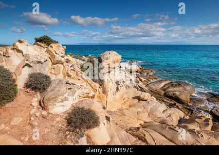 View of the picturesque scene of sea waves crashing on the rocks of a scenic island near resort town in Halkidiki region Stock Photo