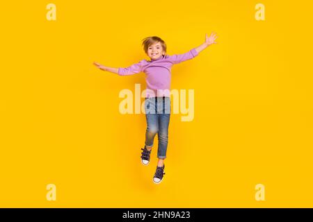 Full size photo of cheerful playful charming boy jumping up waiting summer vacation isolated on yellow color background Stock Photo