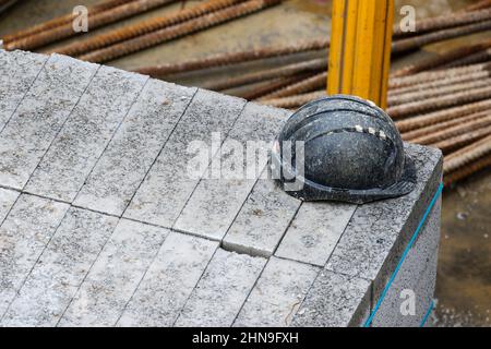 Black hard hat on concrete blocks in construction site. Worn muddy protective equipment or safety wear on rough texture stone. Dublin, Ireland Stock Photo