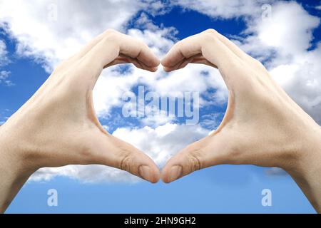 Hands forming heart shape, sky in background - love concept Stock Photo