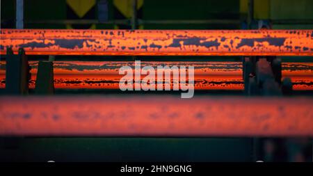 Low depth-of-field. Center in focus. Manufacturing of mild steel square bar on continuous casting machine. Ready hot metal bars. Stock Photo