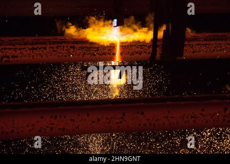 Manufacturing of mild steel square bar on continuous casting machine. Cutting metal by gas torch. Black background. Stock Photo