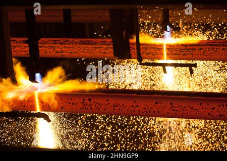 Manufacturing of mild steel square bar on continuous casting machine. Cutting bars by gas torch. Hot bright metal sparks. Stock Photo