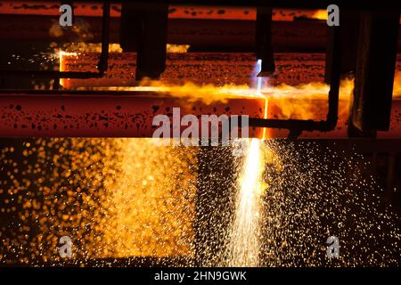 Manufacturing of mild steel square bar on continuous casting machine. Cutting bars by gas torch flame. Metal sparks. Stock Photo