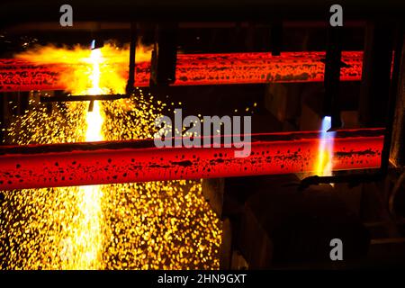 Manufacturing of mild steel square bar on continuous casting machine line. Cutting bars by gas torch. Metal sparks. Stock Photo