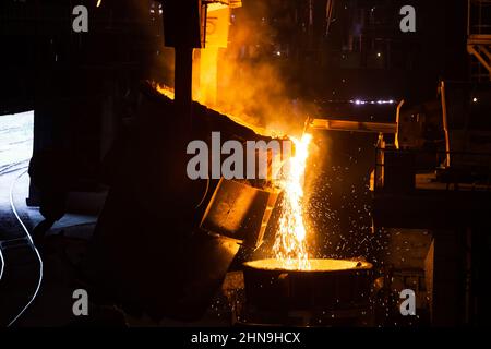 Molten metal pouring from metallurgy ladle. Smoke, on black background. Stock Photo