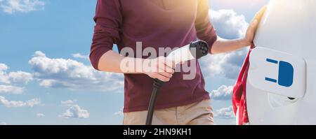 Man holding electric car charging cable on a background of blue sky Stock Photo