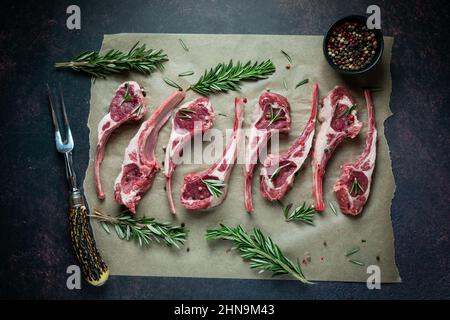 Raw lamb chops on parchment paper with rosemary and peppercorns. Stock Photo