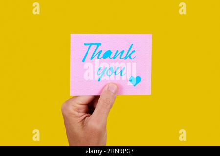 closeup of a man with a pink piece of paper with the text thank you written in blue, on a yellow background Stock Photo