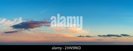 Pastel colored scenic skyscape at sunset. Vanilla sky. Pink and dark blue clouds low on the horizon against clear azure sky at evening. Wide panorama. Stock Photo